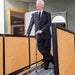 Man in a suit standing in an office setting with wooden partitions.