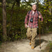 Man hiking in a forest wearing a red plaid shirt and carrying a camera.