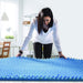 Woman examining a blue foam mattress topper in a room.