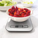 Bowl of sliced strawberries on a digital kitchen scale with ingredients in the background