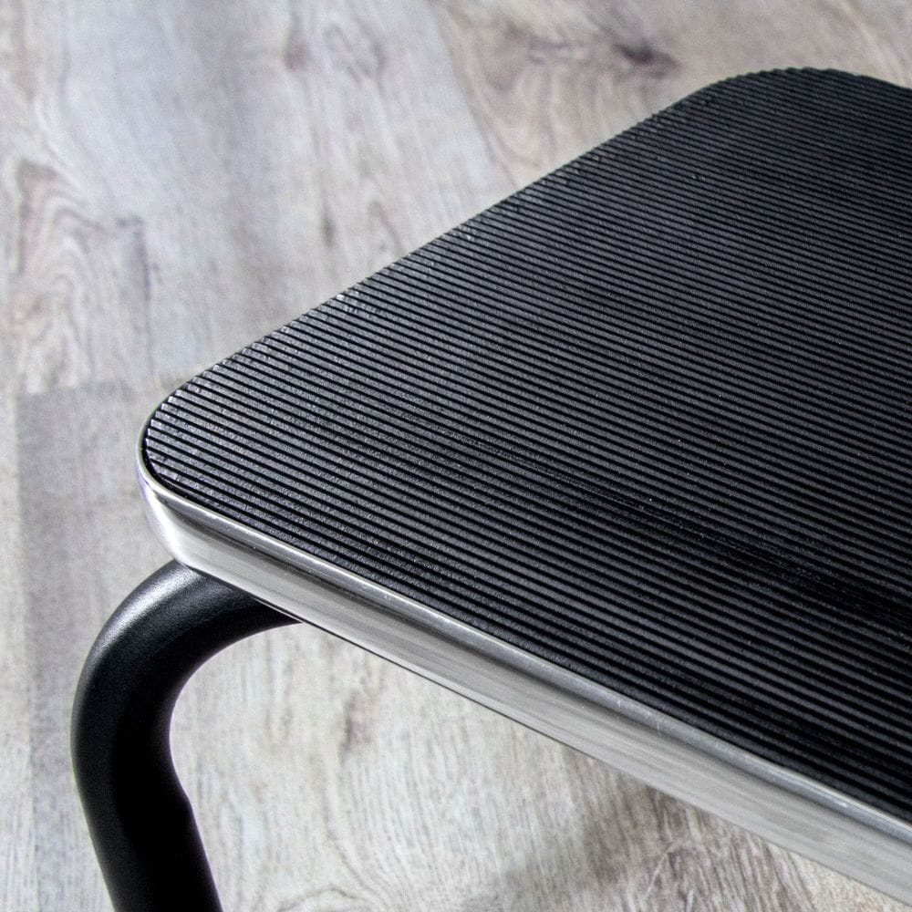 Close-up of a black metal footstool on a light wood floor.