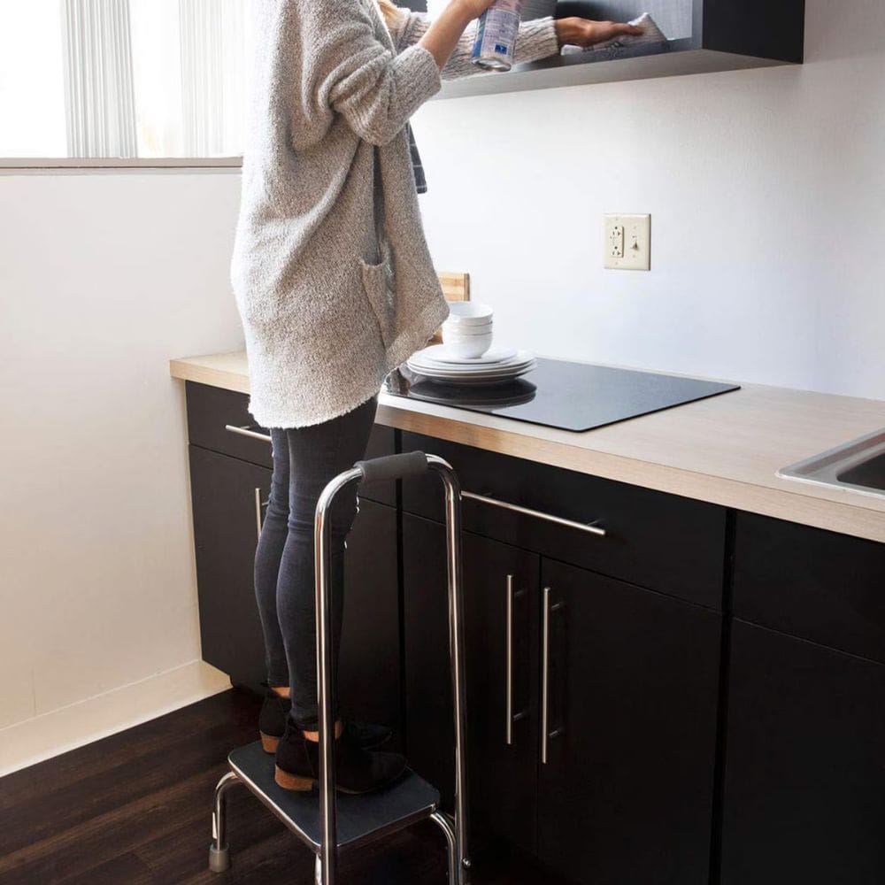 Person using a step stool to reach a high cabinet in a kitchen.
