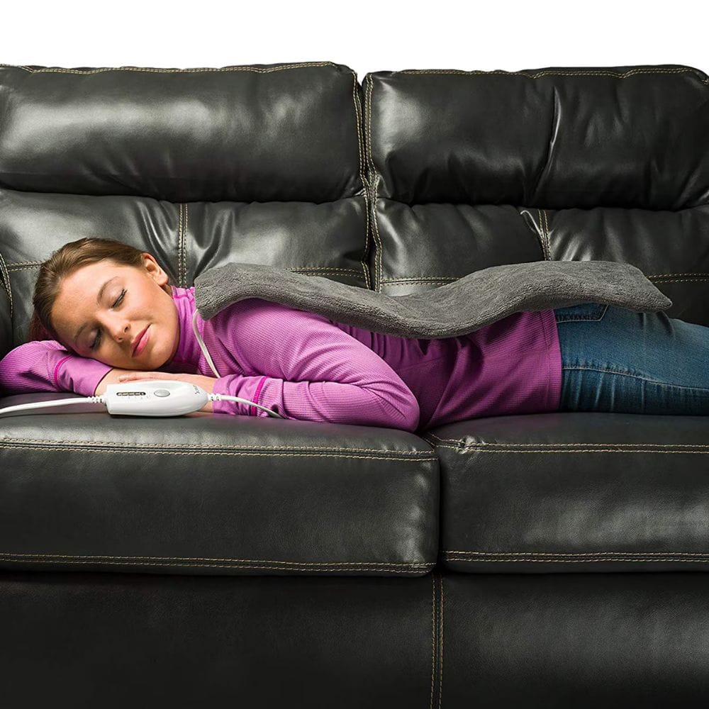Person lying on a black leather couch with a gray blanket and white device.