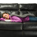 Person lying on a black leather couch with a gray blanket and white device.