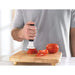 Person using a tomato peeler on a wooden cutting board with tomatoes