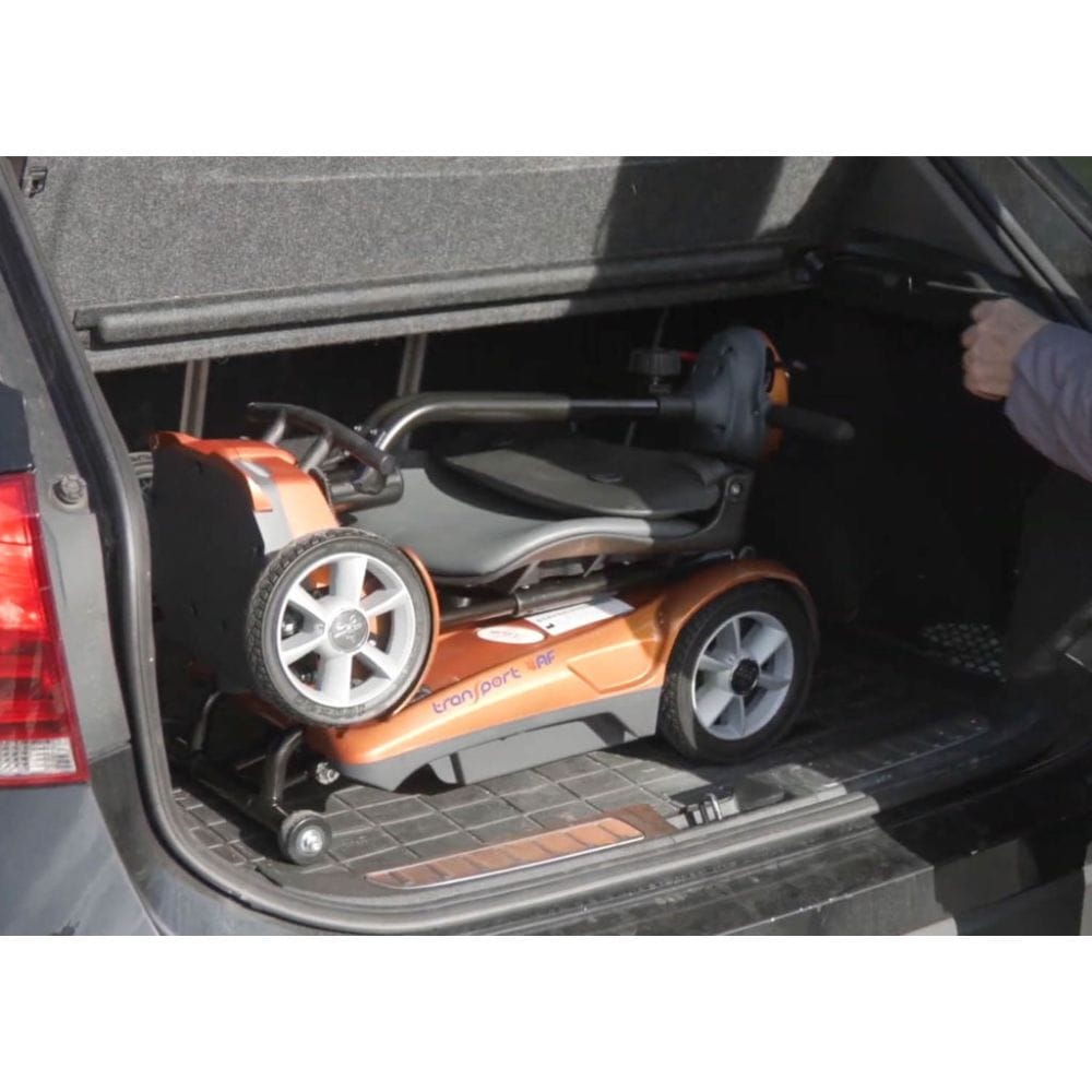 Orange and gray lawn mower being loaded into a car trunk.