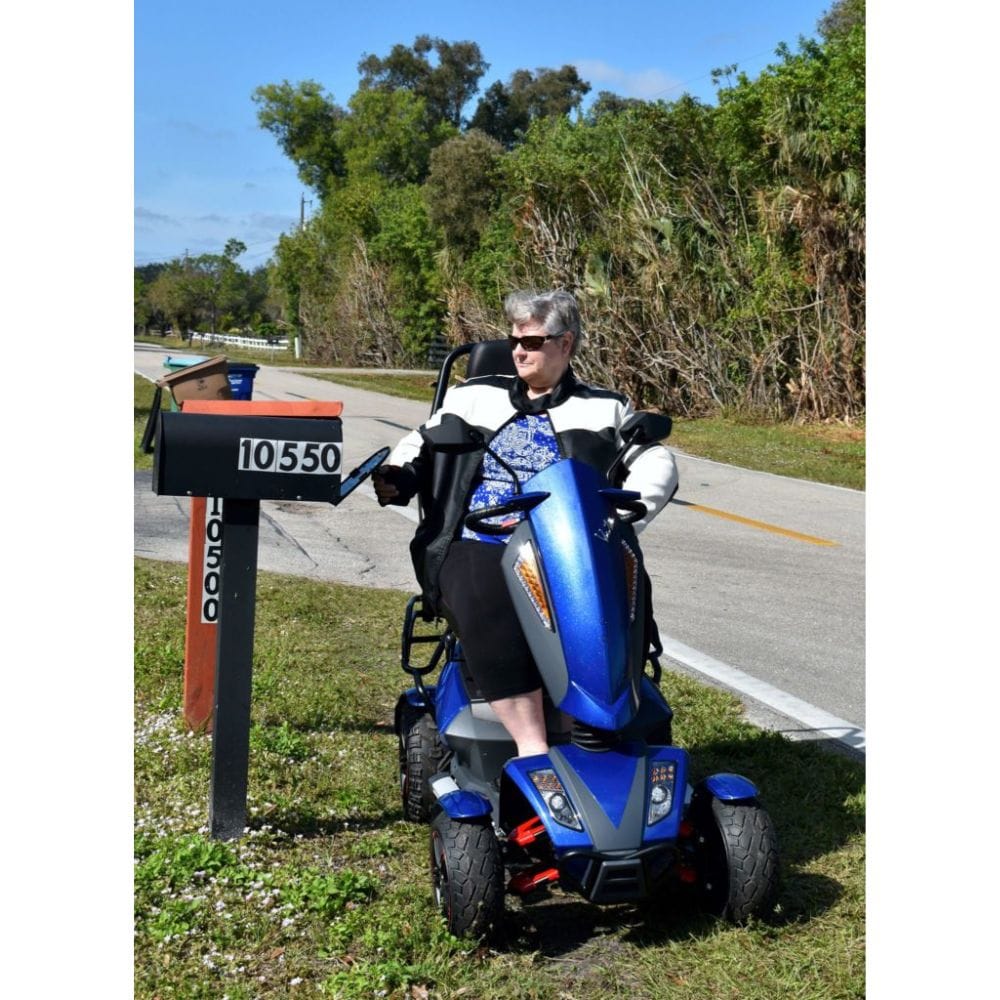 Person riding a blue mobility scooter near a mailbox on a road with trees in the background
