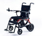 Monarch Mobility Ezi-Fold Carbon power wheelchair with black seating, orange frame accents, joystick control, and swing-away footrests.