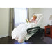 Woman reading a book in a recliner chair with white bedding in a room.