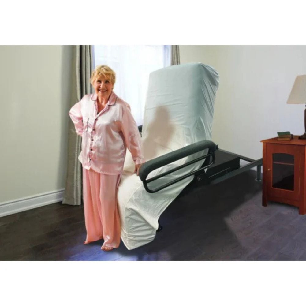 Woman in pink pajamas standing next to a bed with a mattress cover in a bedroom.