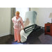 Woman in pink pajamas standing next to a bed with a mattress cover in a bedroom.