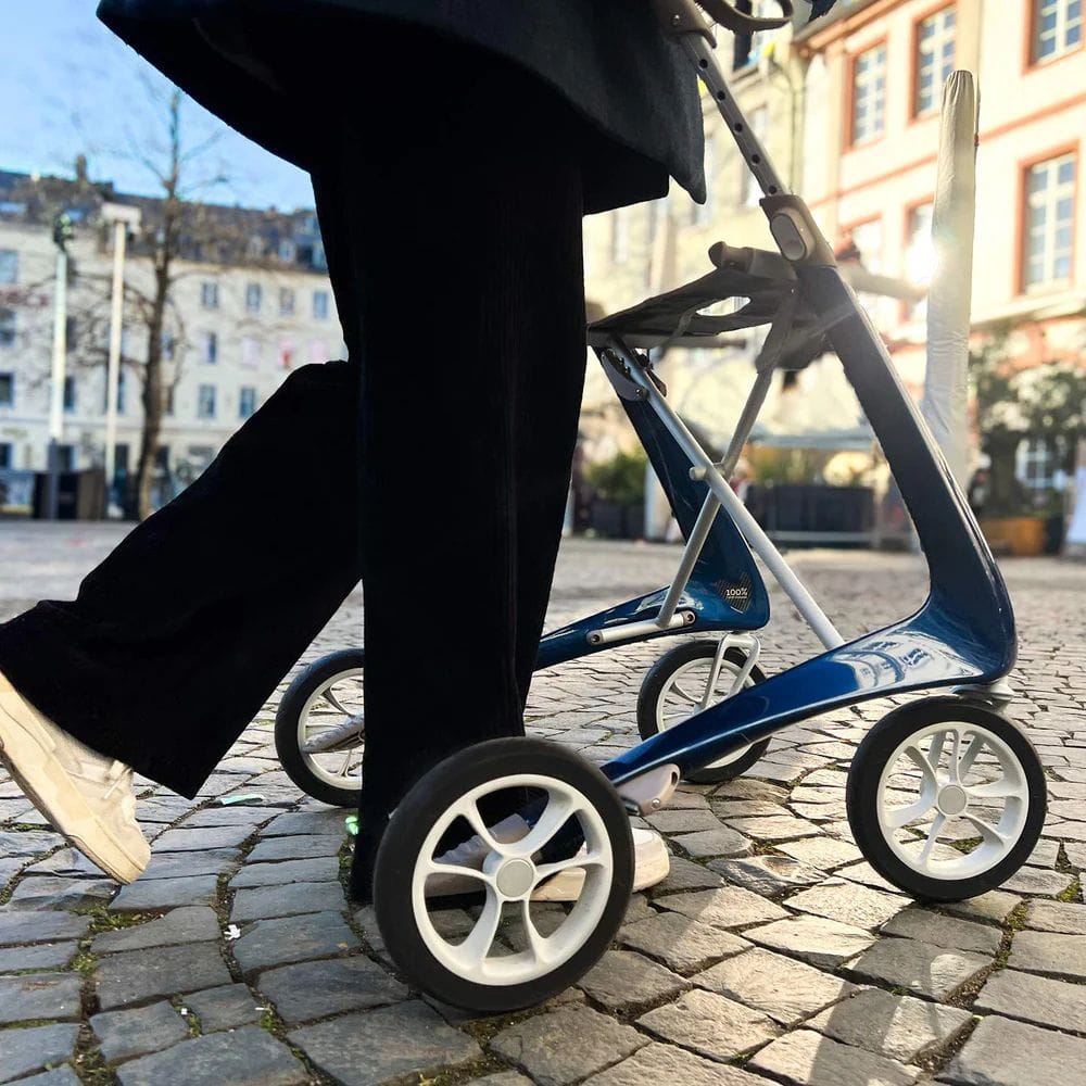 Person pushing a blue stroller on a cobblestone street with buildings in the background