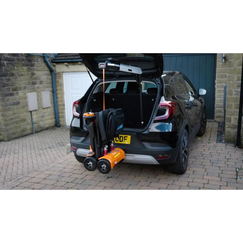 Black car with open trunk and orange and black towing device attached, parked in front of a garage.