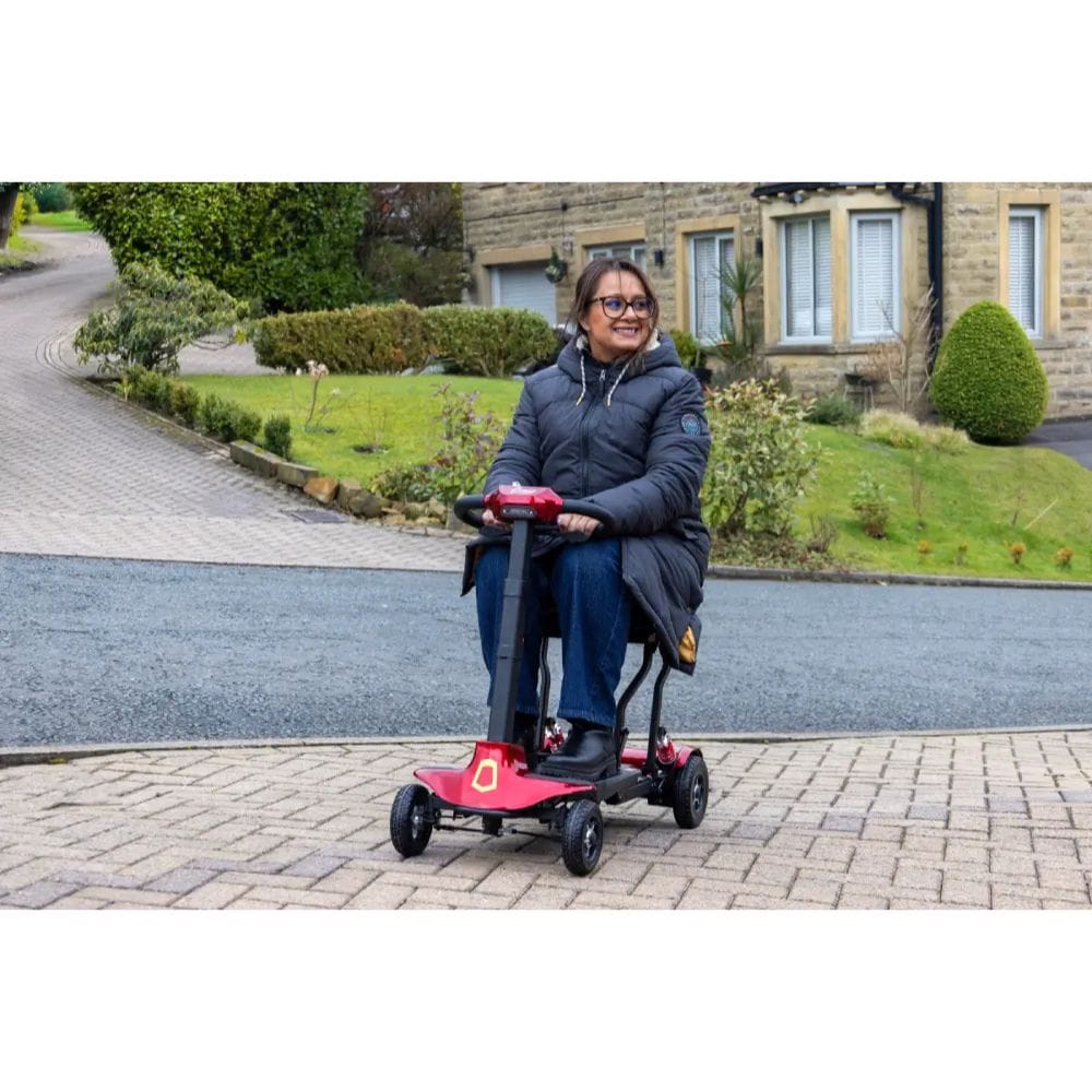 Person using a red mobility scooter on a driveway with a house in the background