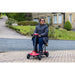 Person using a red mobility scooter on a driveway with a house in the background