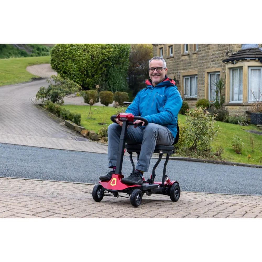 Man riding a mobility scooter on a driveway with a house in the background