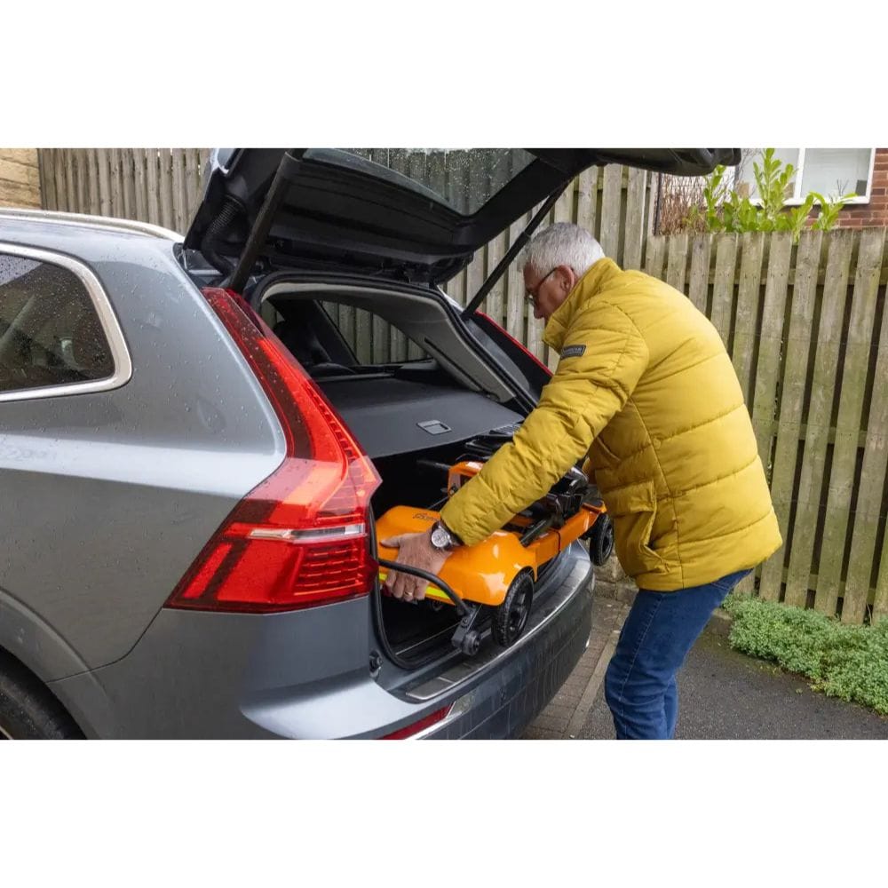 Person loading a yellow lawnmower into the trunk of a gray car.