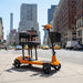 Orange electric scooter on a city street with tall buildings in the background