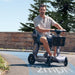 Man riding a mobility scooter on a road with trees in the background