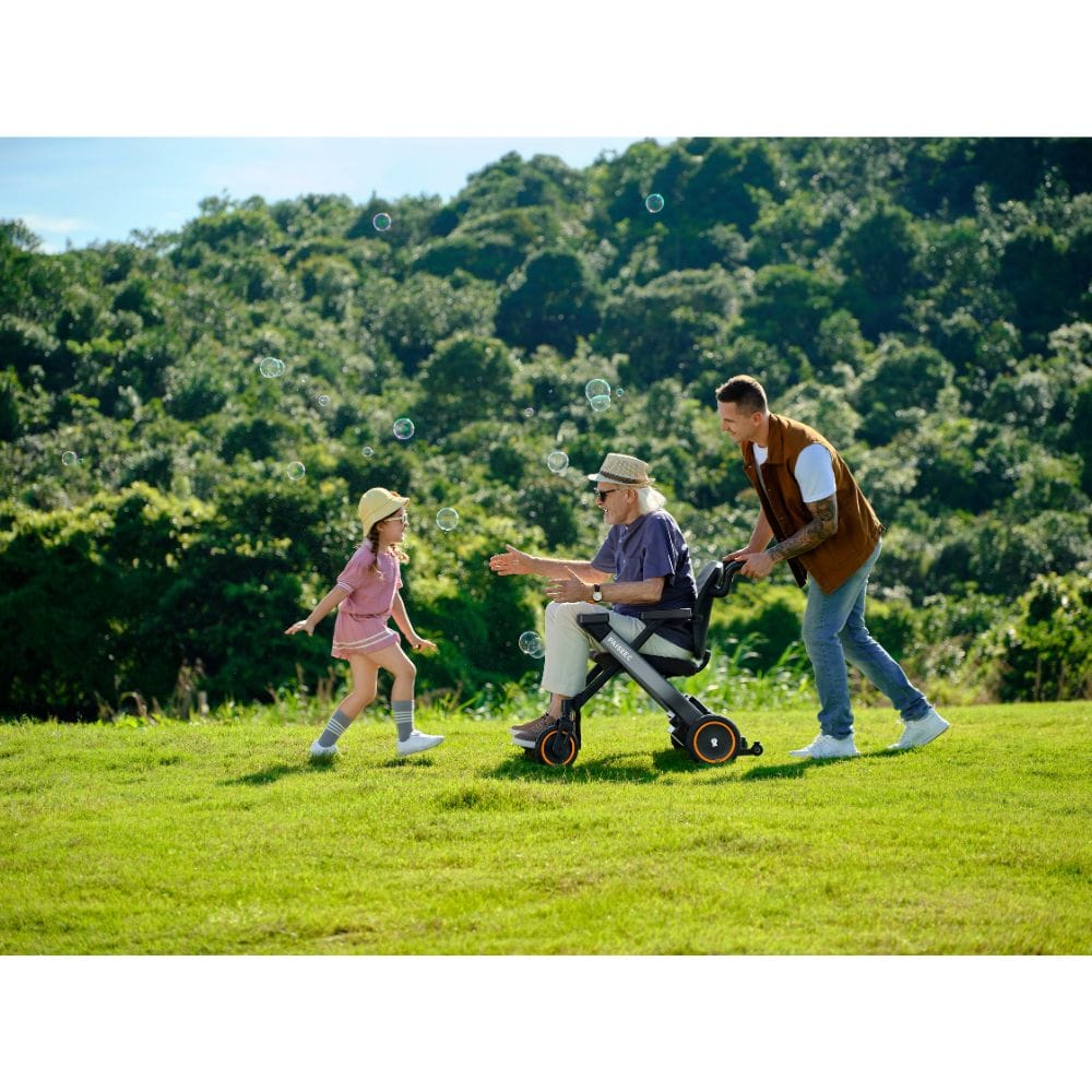 Man pushing a child in a stroller with a young girl running alongside, all in a lush green field.
