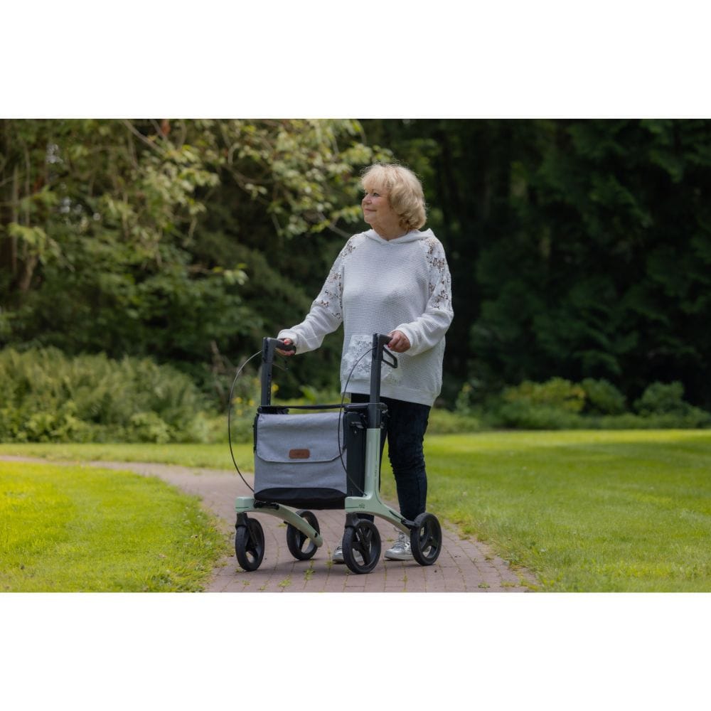 Woman pushing a mobility scooter with a bag on a path in a park.