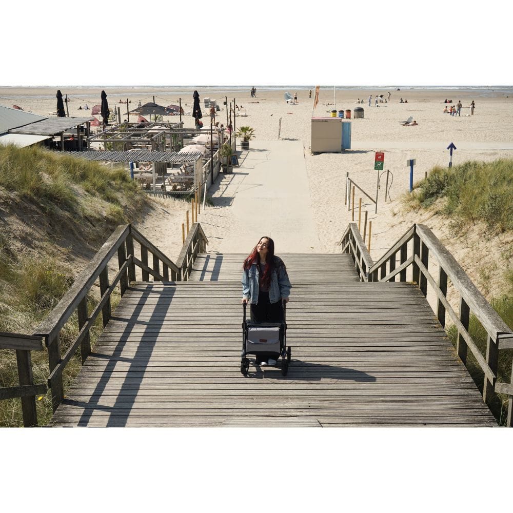 Woman pushing a stroller up a wooden staircase towards a beach.