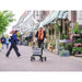 Woman pushing a stroller on a street with shops and plants in the background
