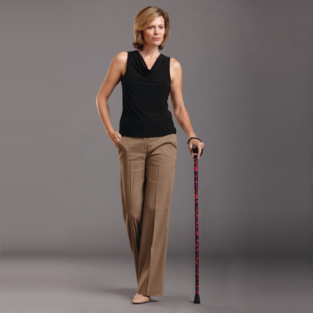 Woman in black sleeveless top and brown pants holding a walking cane on a gray background