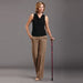 Woman in black sleeveless top and brown pants holding a walking cane on a gray background