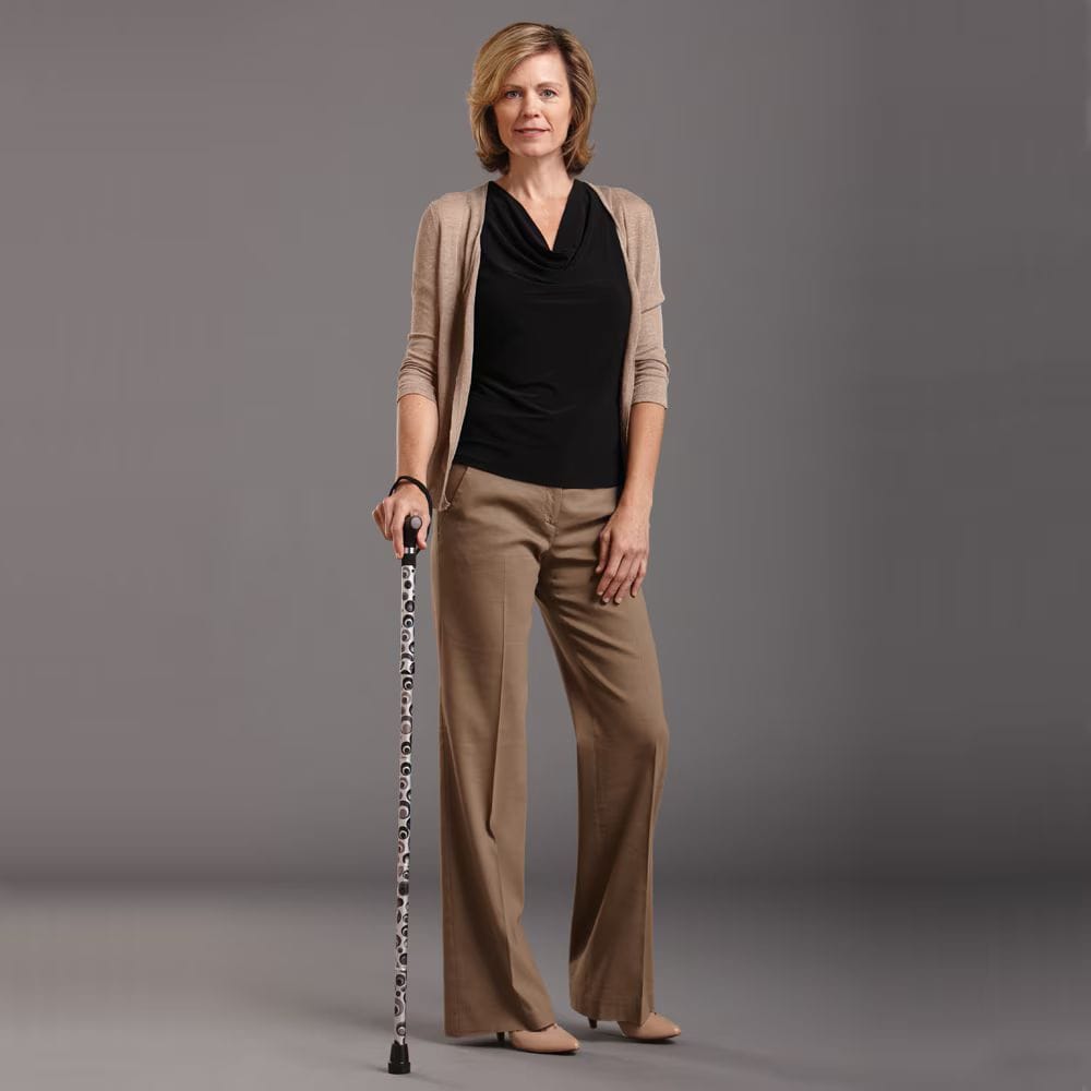 Woman in brown outfit holding a cane against a gray background