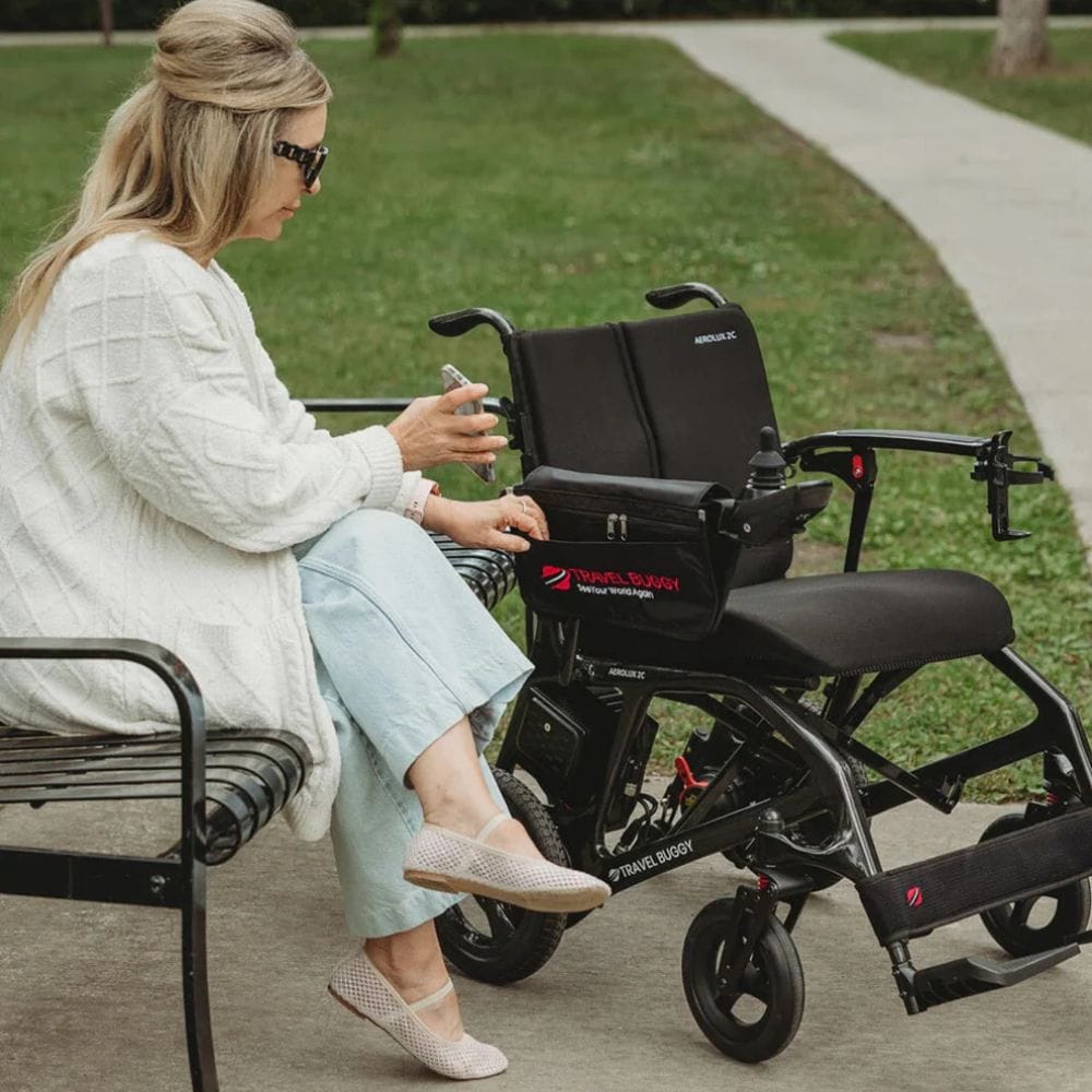 Woman sitting on a bench with a black electric wheelchair next to her.
