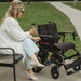 Woman sitting on a bench with a black electric wheelchair next to her.