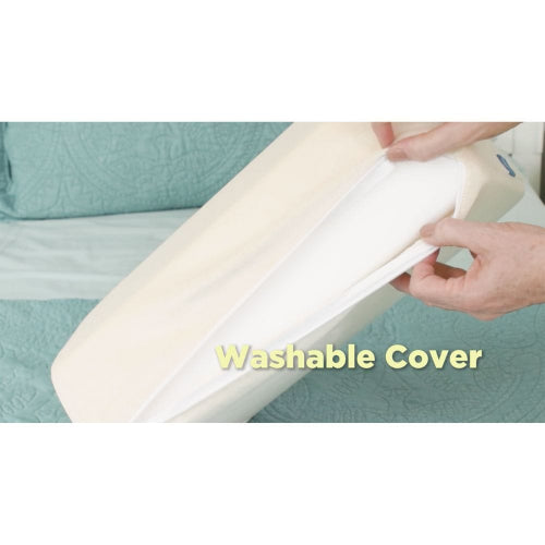 A close-up of a person's hands peeling back a white washable cover from a cream-colored mattress topper or pillow, with a teal quilted bedspread in the background and the text 'Washable Cover' overlaid in yellow.